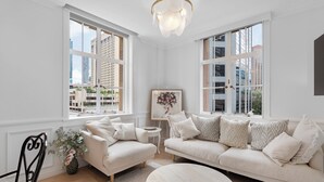A spacious living room with a large sofa, a round coffee table, and a chair. There are two large windows providing a view of the cityscape. - Rothbury Hotel (Brisbane)