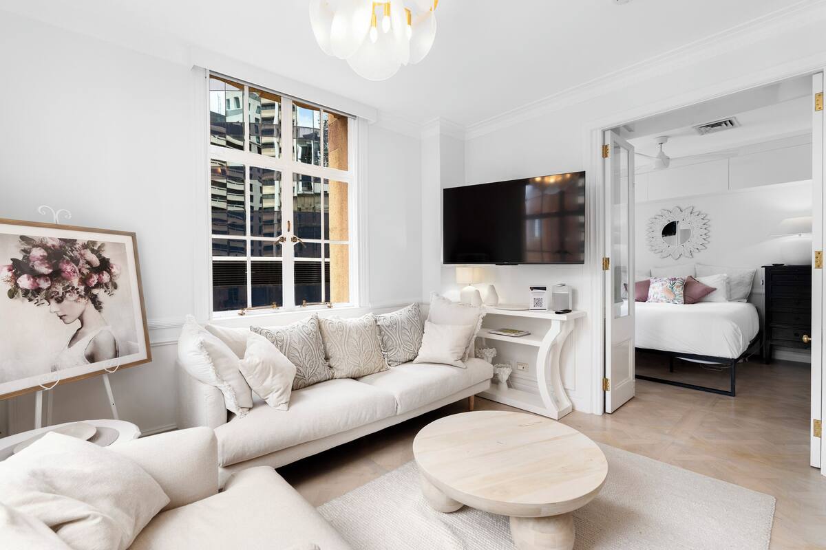 A modern, well-lit living room with a large window, a sofa, a coffee table, and a flat-screen TV.
