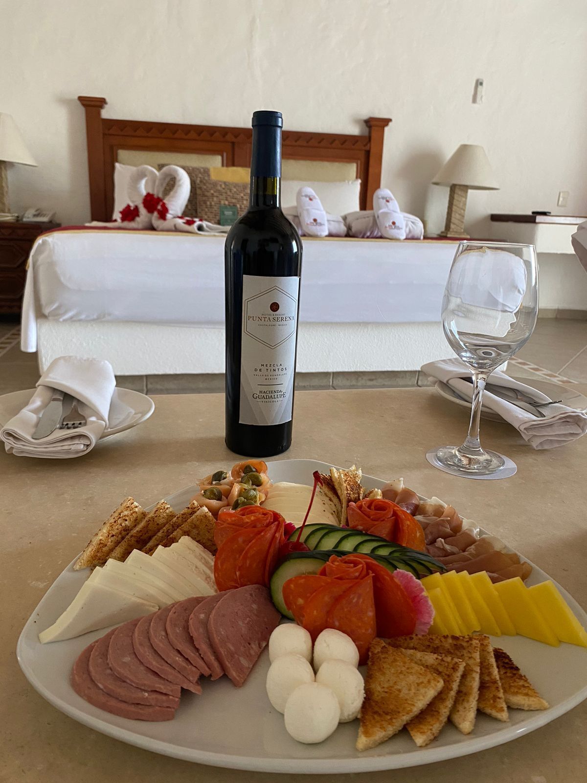 Habitación de hotel con una bandeja de desayuno ordenada, una botella de vino y una cama con cabecero de madera.