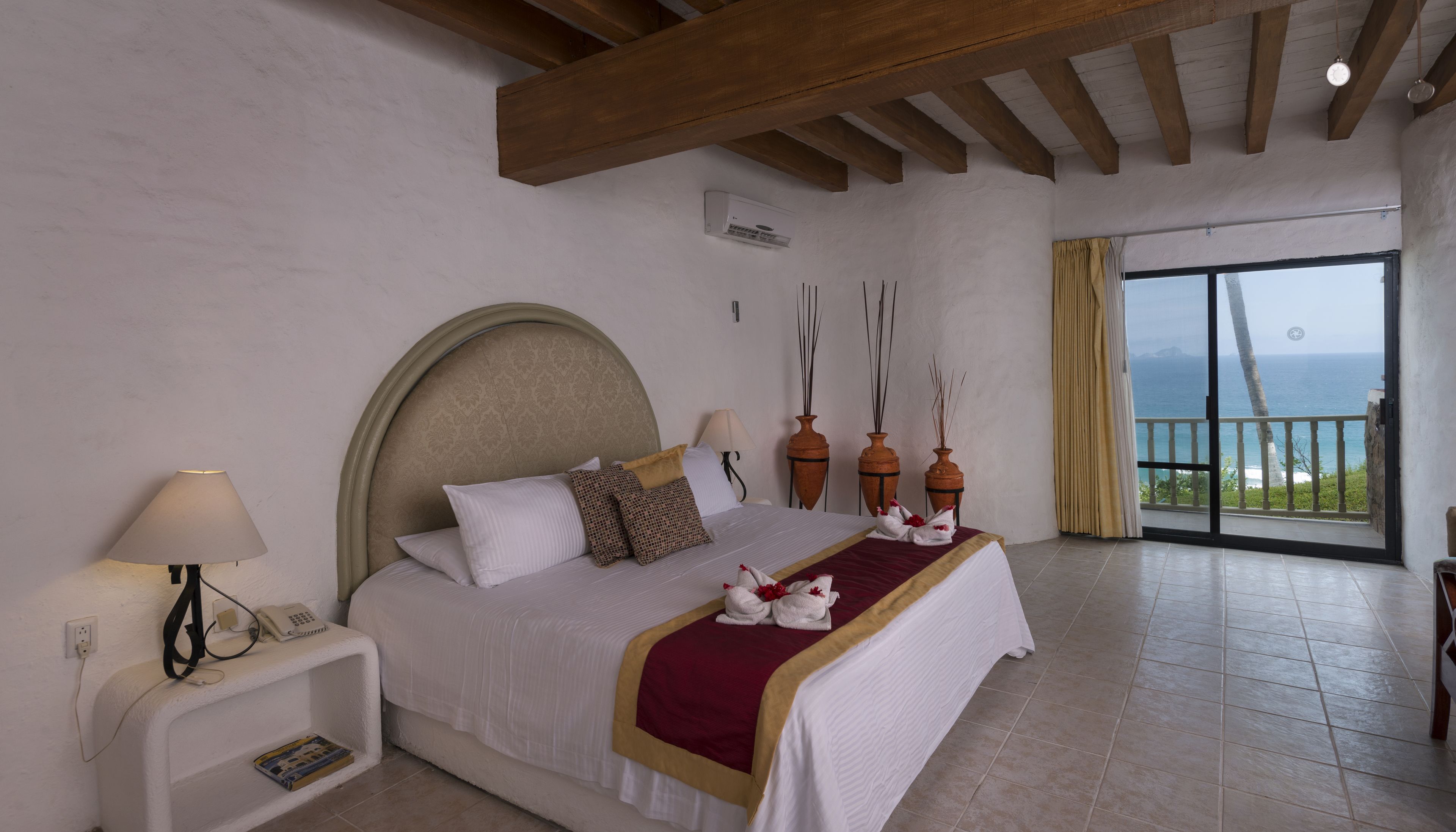 A hotel room with a bed, bedside table, lamp, and a view of the ocean through a balcony.