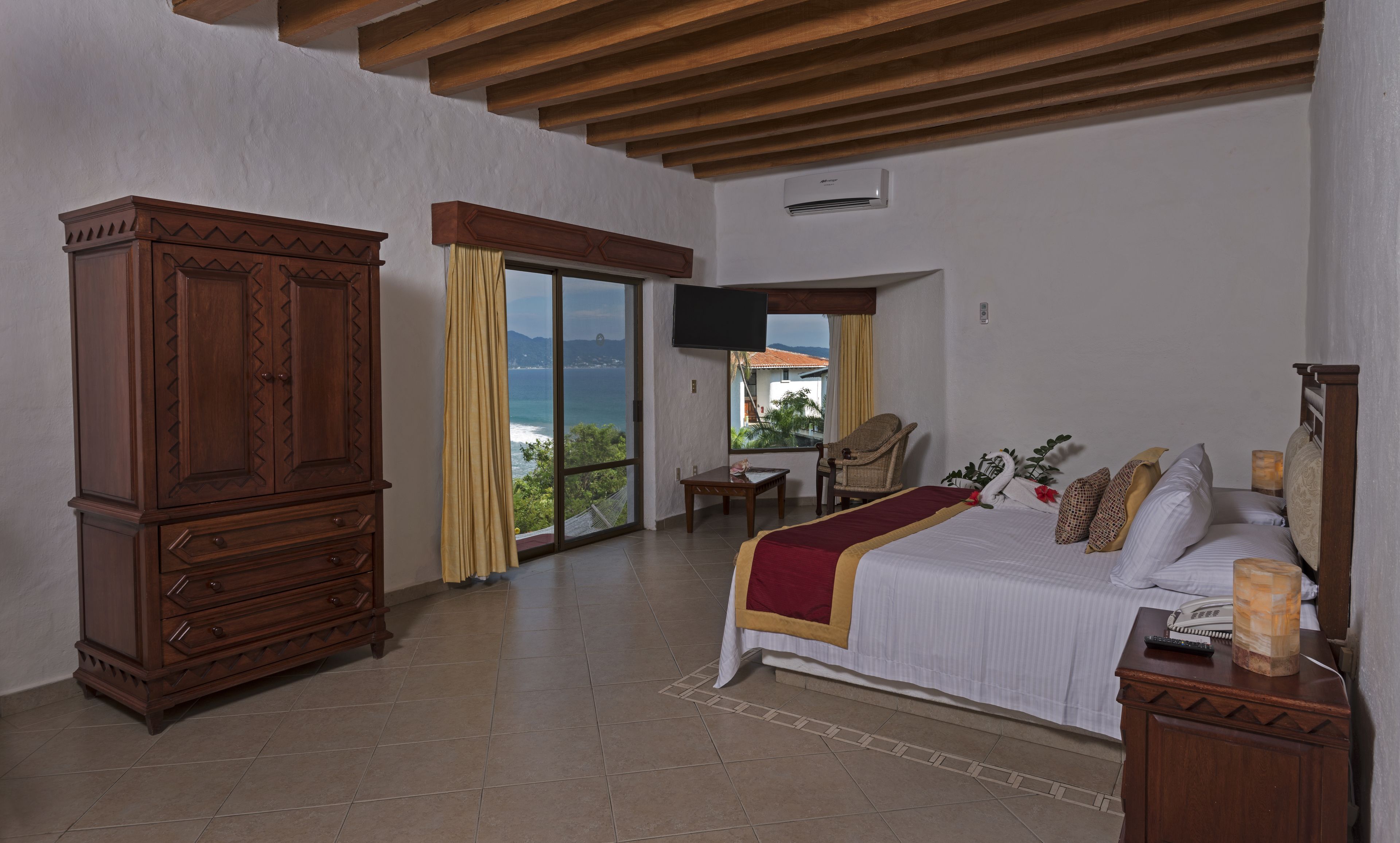 Quarto com cama grande, guarda-roupa de madeira e televisão na parede.