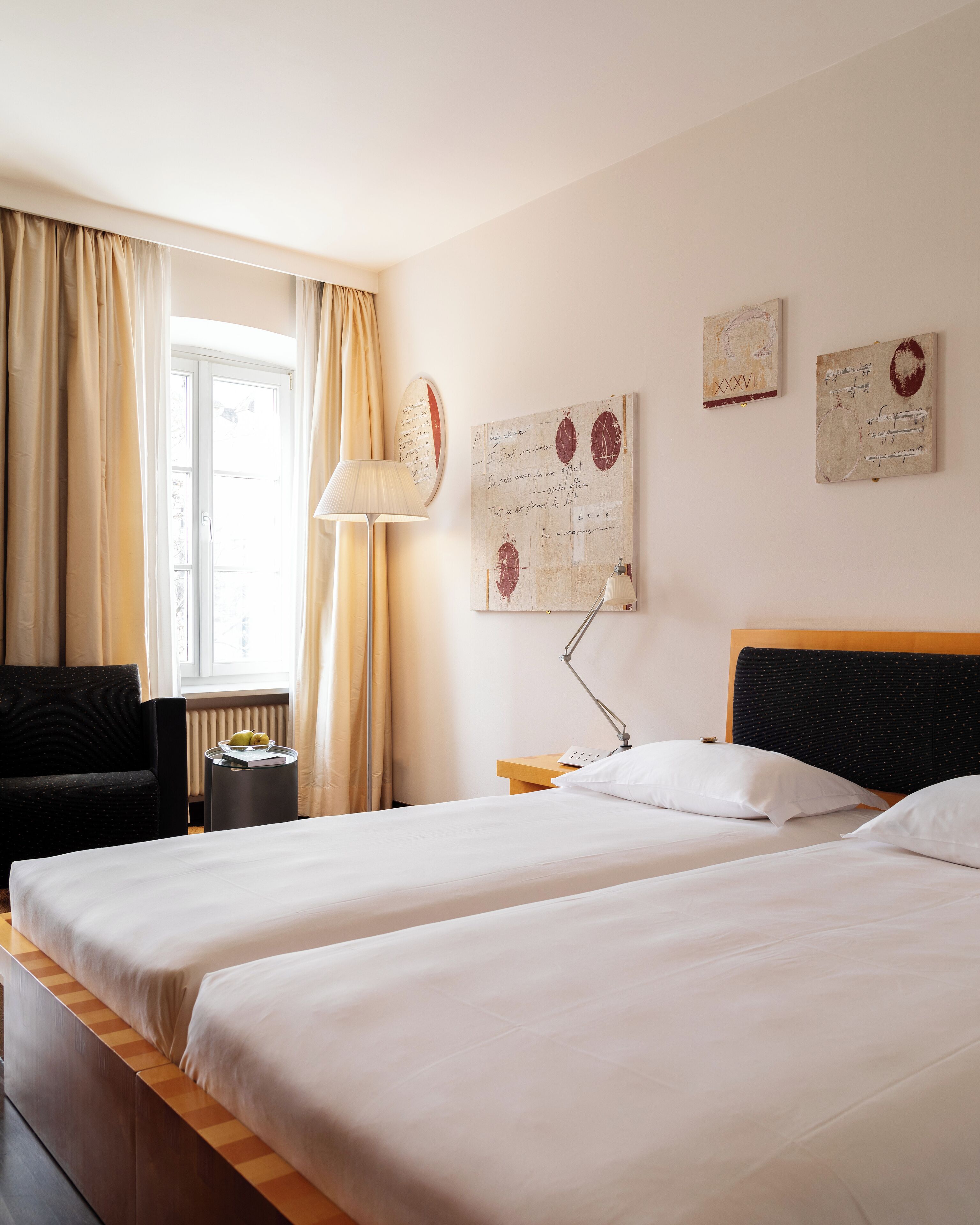 Una camera d'albergo con due letti, una scrivania, una sedia e opere d'arte alle pareti.