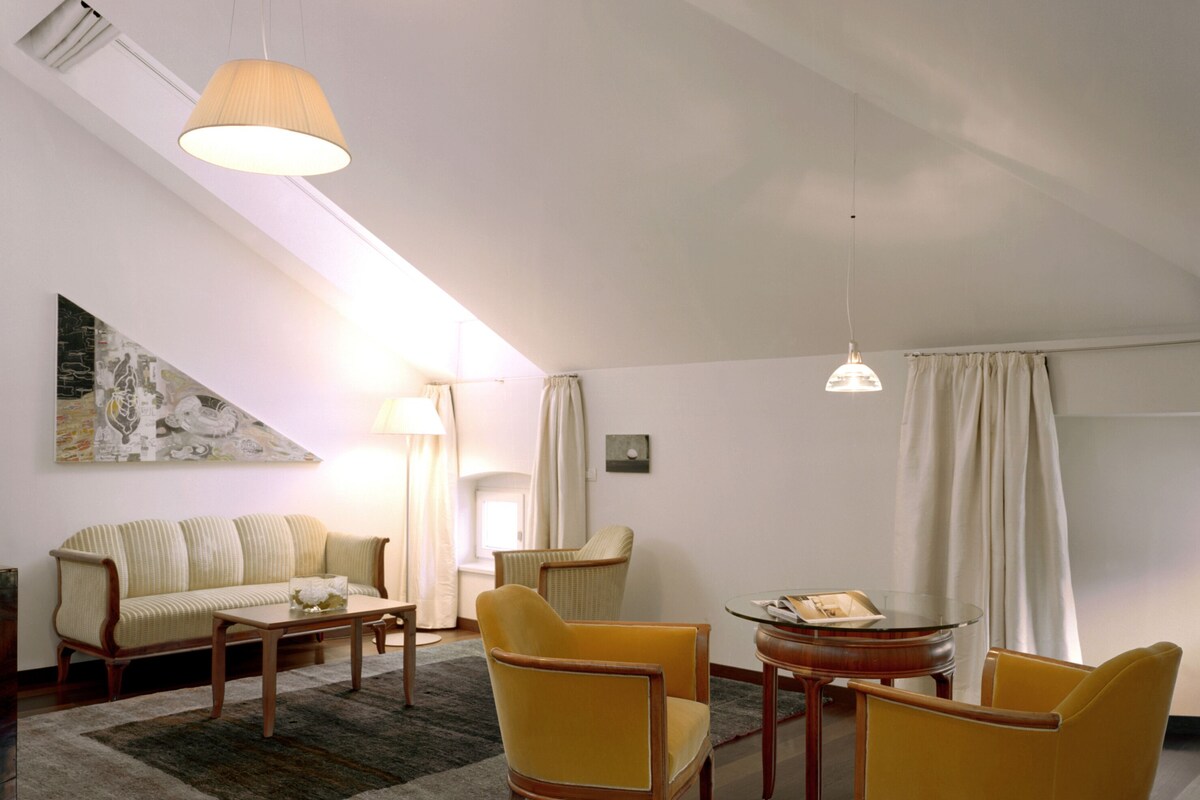 A spacious living room with a sofa, two yellow armchairs, a coffee table, and a glass-top table.