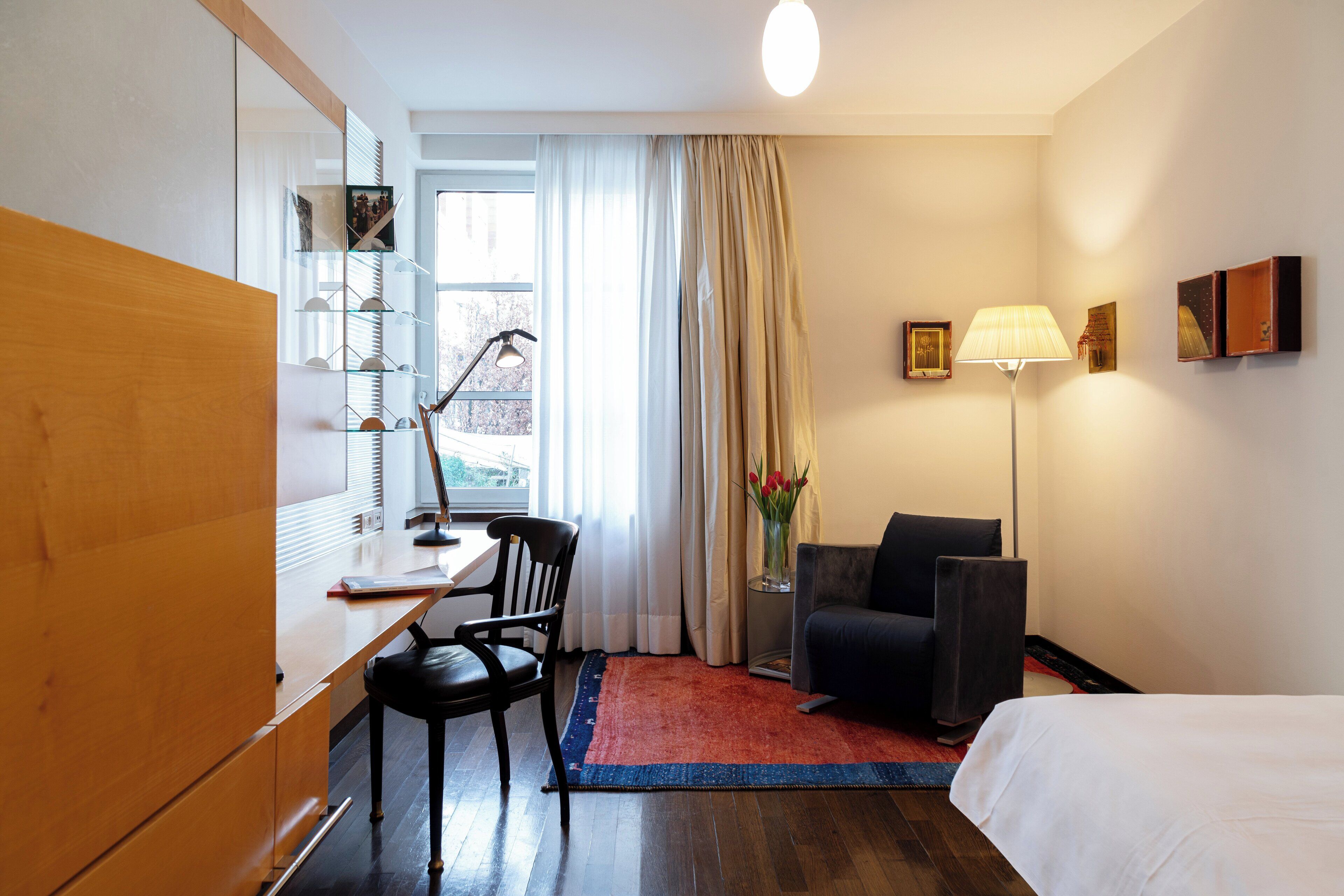 Ett hotellrum med en säng, ett skrivbord med en stol, en lampa och ett fönster med gardiner.