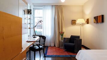 Ett hotellrum med en säng, ett skrivbord med en stol, en lampa och ett fönster med gardiner.