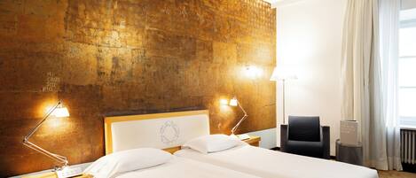 Een hotelkamer met twee bedden, een houten hoofdbord, een nachtkastje met een lamp, een stoel en uitzicht op de omgeving.
