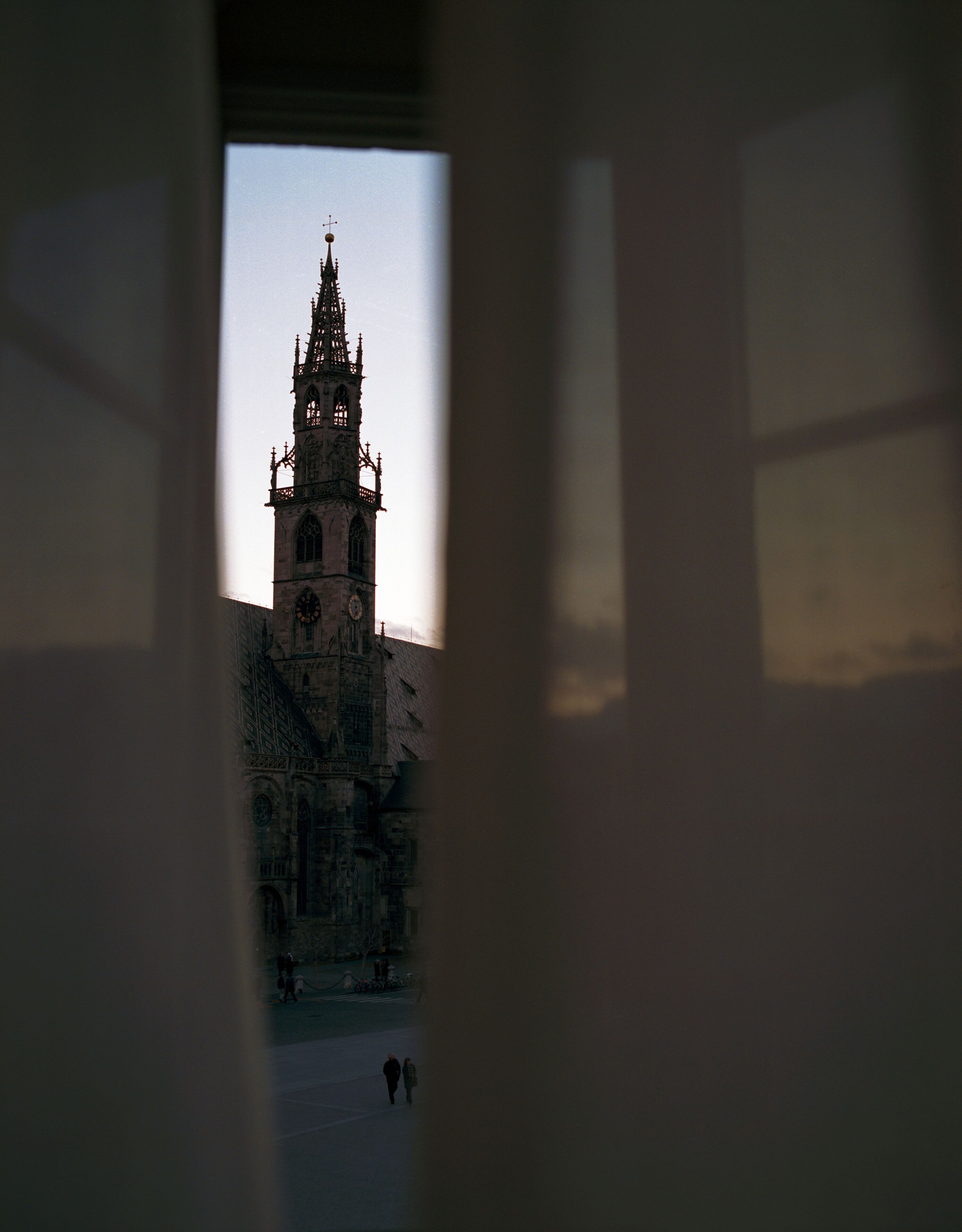 Blick durch ein Fenster auf ein historisches Gebäude mit aufwendiger Architektur, darunter ein hoher Turm und detaillierte Steinmetzarbeiten.