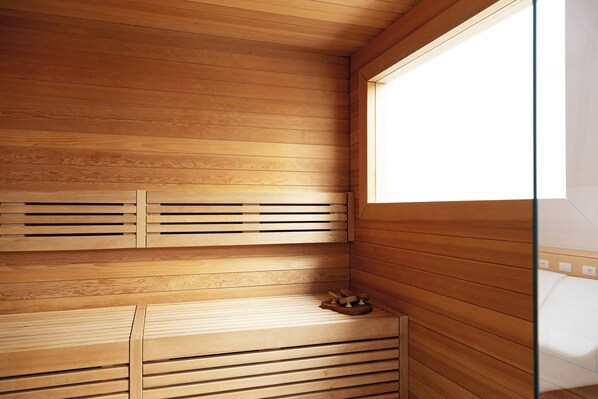 Una sala de sauna con listones de madera en el techo y las paredes, un banco y una pequeña estructura de madera.