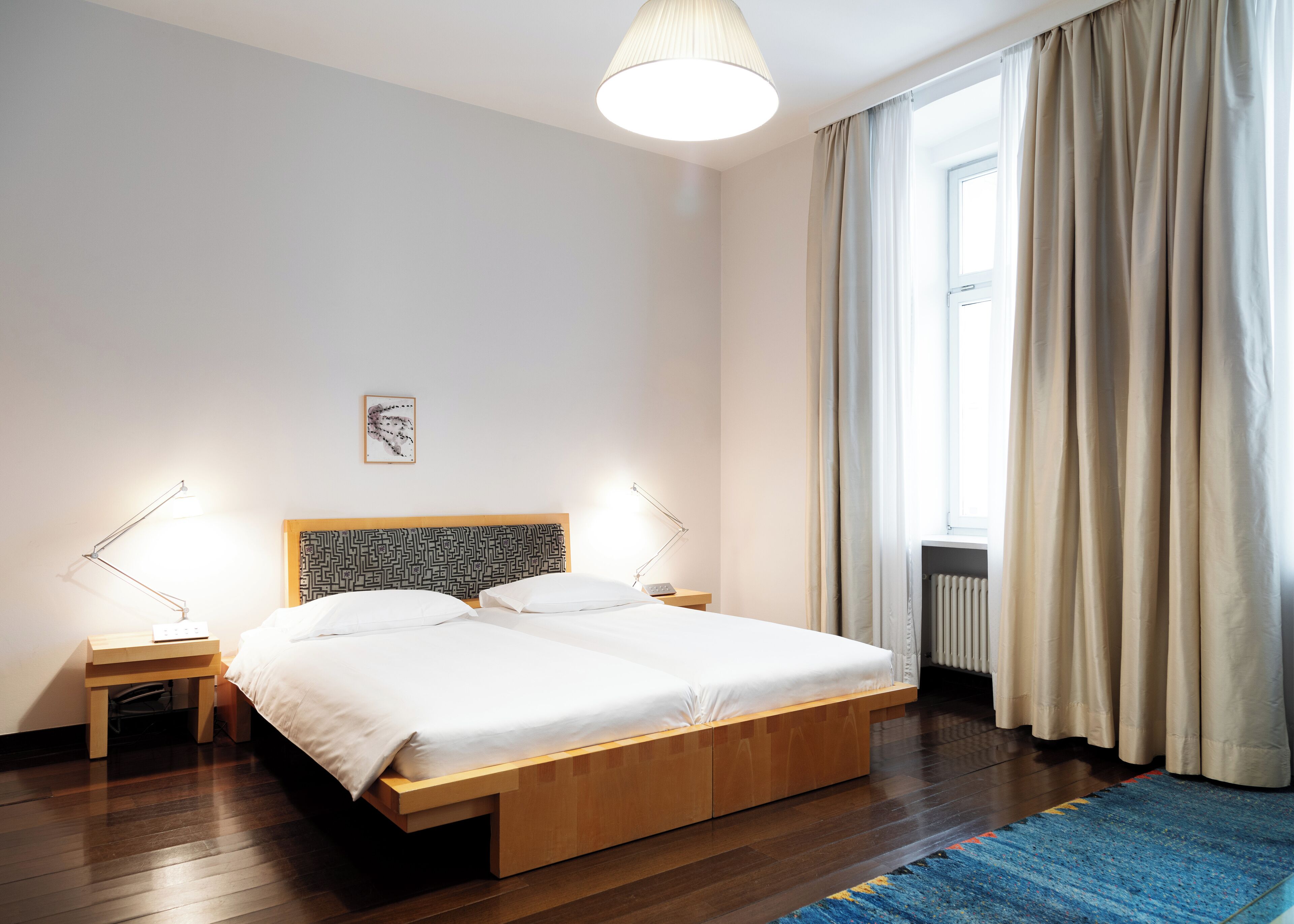 Een moderne slaapkamer met een houten bed, twee nachtkastjes, een vloerlamp, een raam met gordijnen en een radiator.