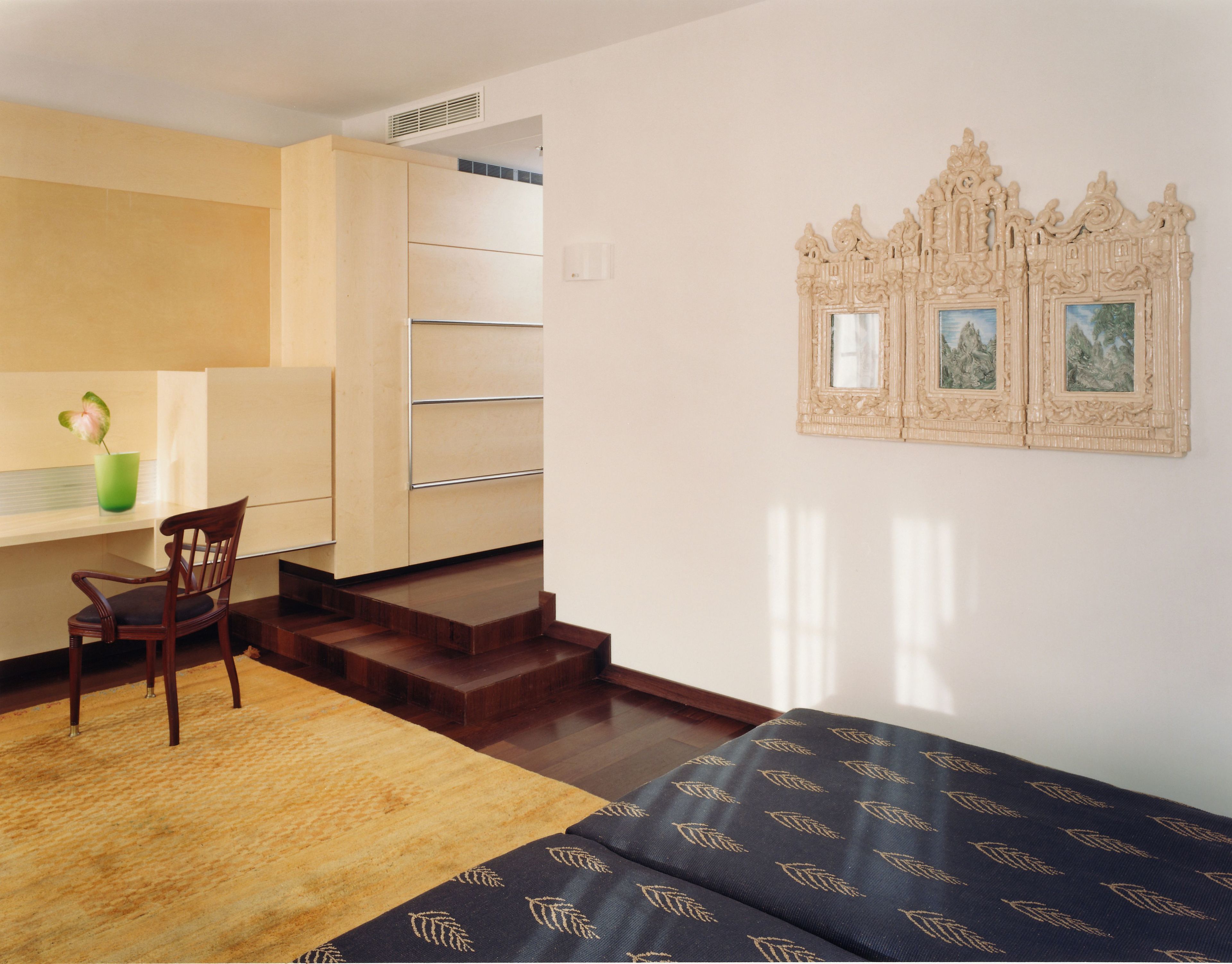A modern room with a bed, a desk, and a chair. There is a staircase leading to an upper level.