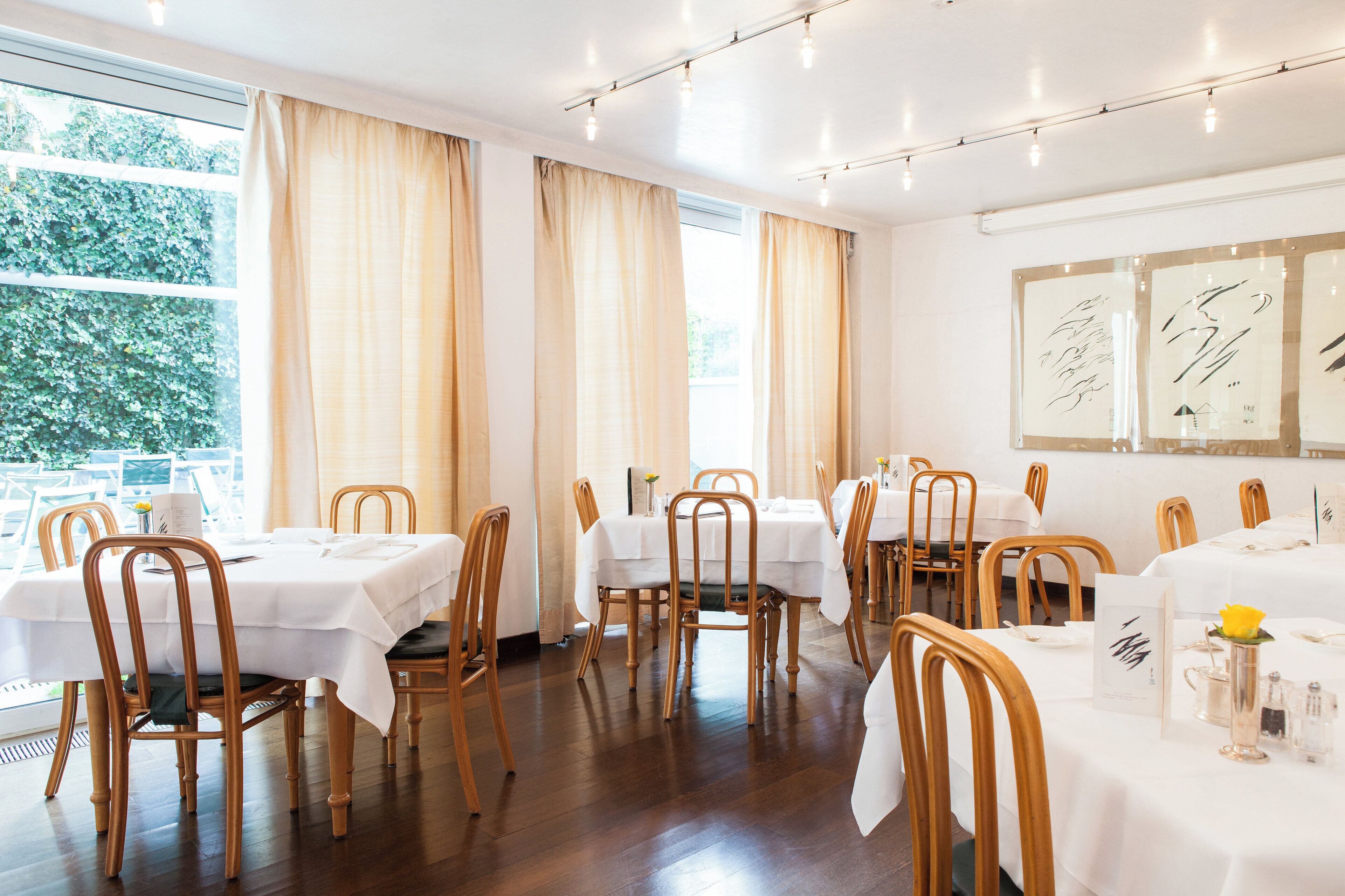 Un restaurante con varias mesas, sillas de madera y vistas a espacios verdes.