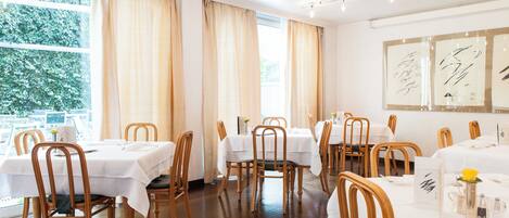 Un restaurante con varias mesas, sillas de madera y vistas a espacios verdes.
