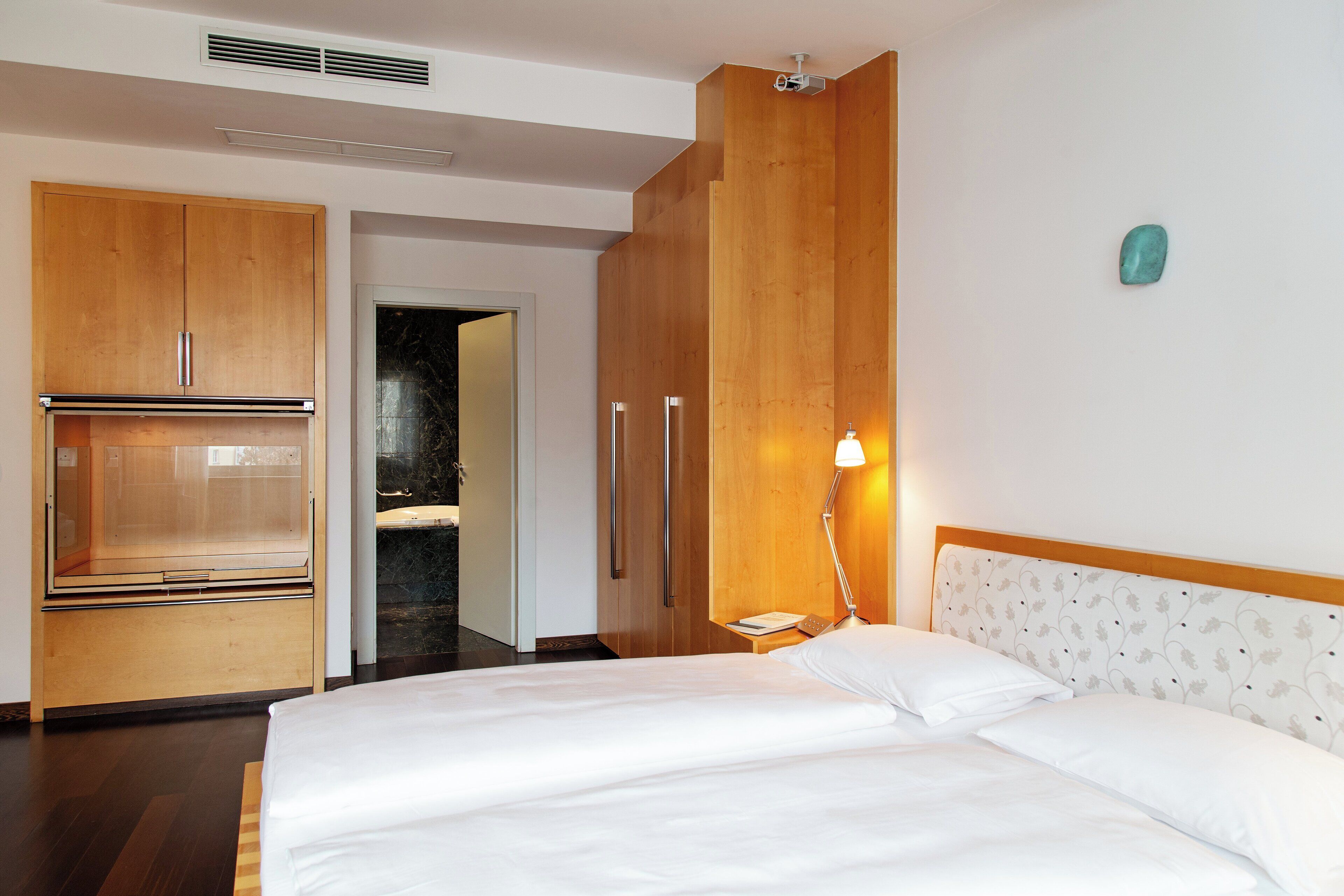 A hotel room with a bed, wooden wardrobe, and a nightstand with a lamp.