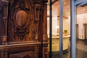 Un mostrador de recepción de madera con intrincados grabados, un acceso por puerta de cristal y un interior moderno con una zona de estar circular.