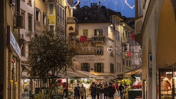 Una stretta via fiancheggiata da edifici, con un albero al centro e persone che camminano.