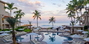 Une piscine d’hôtel avec des chaises longues et des parasols, des palmiers et une vue sur l’océan.