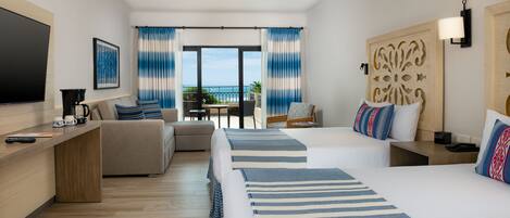 A hotel room with a large bed, a sofa, a desk with a coffee maker, and a view of the ocean.