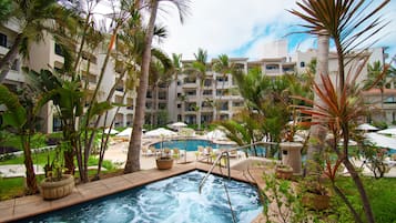 Zona de piscina de hotel con jacuzzi, rodeada de palmeras y sillones de descanso.