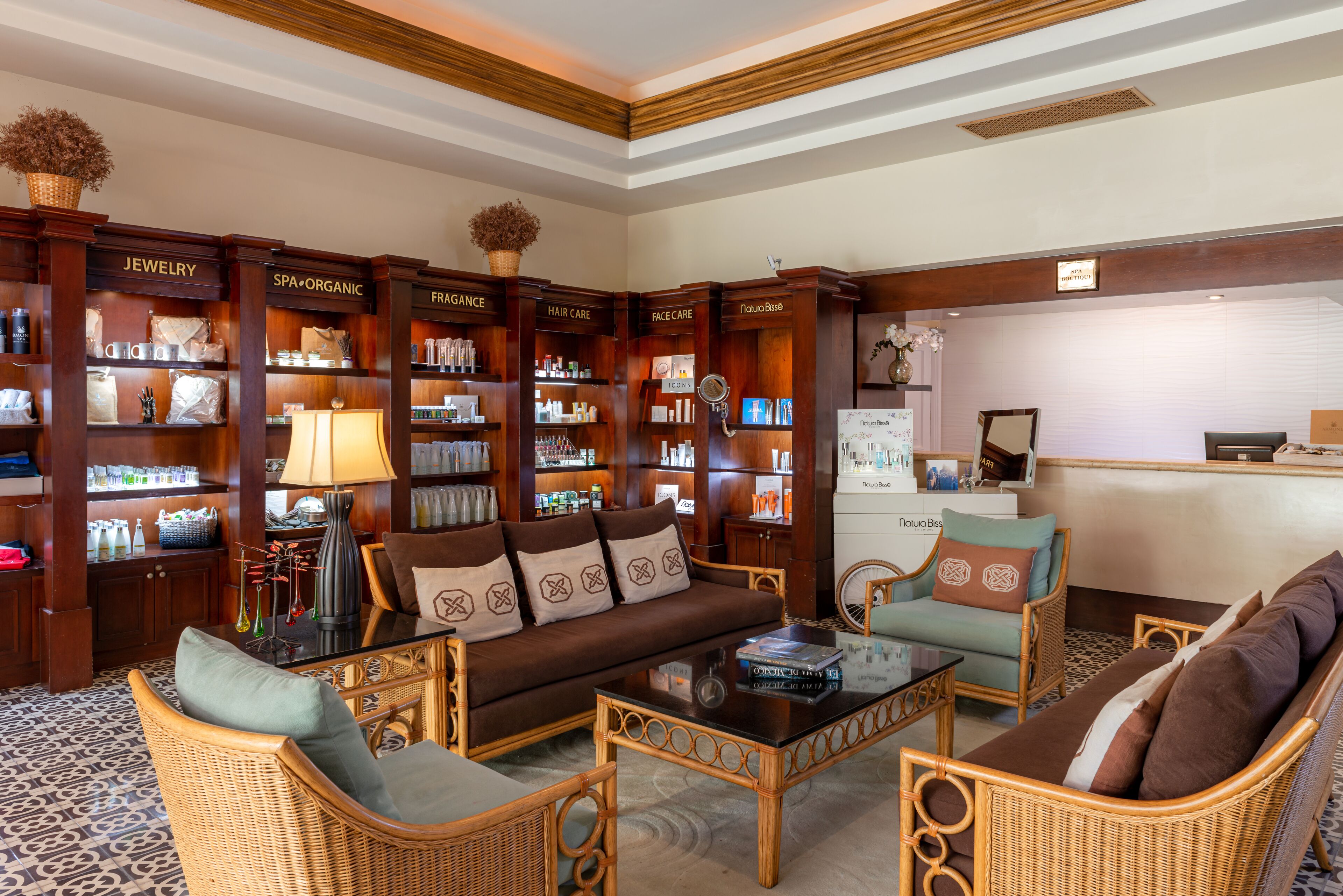 A hotel lobby with a central seating area, wooden bookshelves labeled with categories like 'JEWELRY' and 'SPA', and a reception desk.