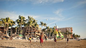 A beach with palm trees, beach umbrellas, and a building with multiple balconies.