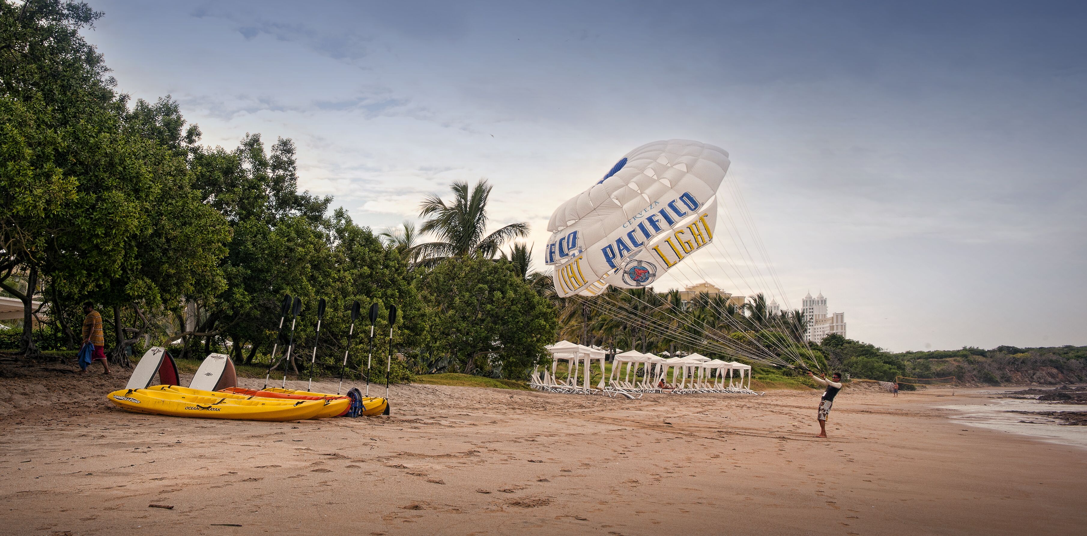 Una playa con kayak, paracaídas y sombrillas.