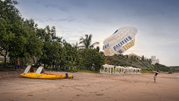 Una playa con kayak, paracaídas y sombrillas.