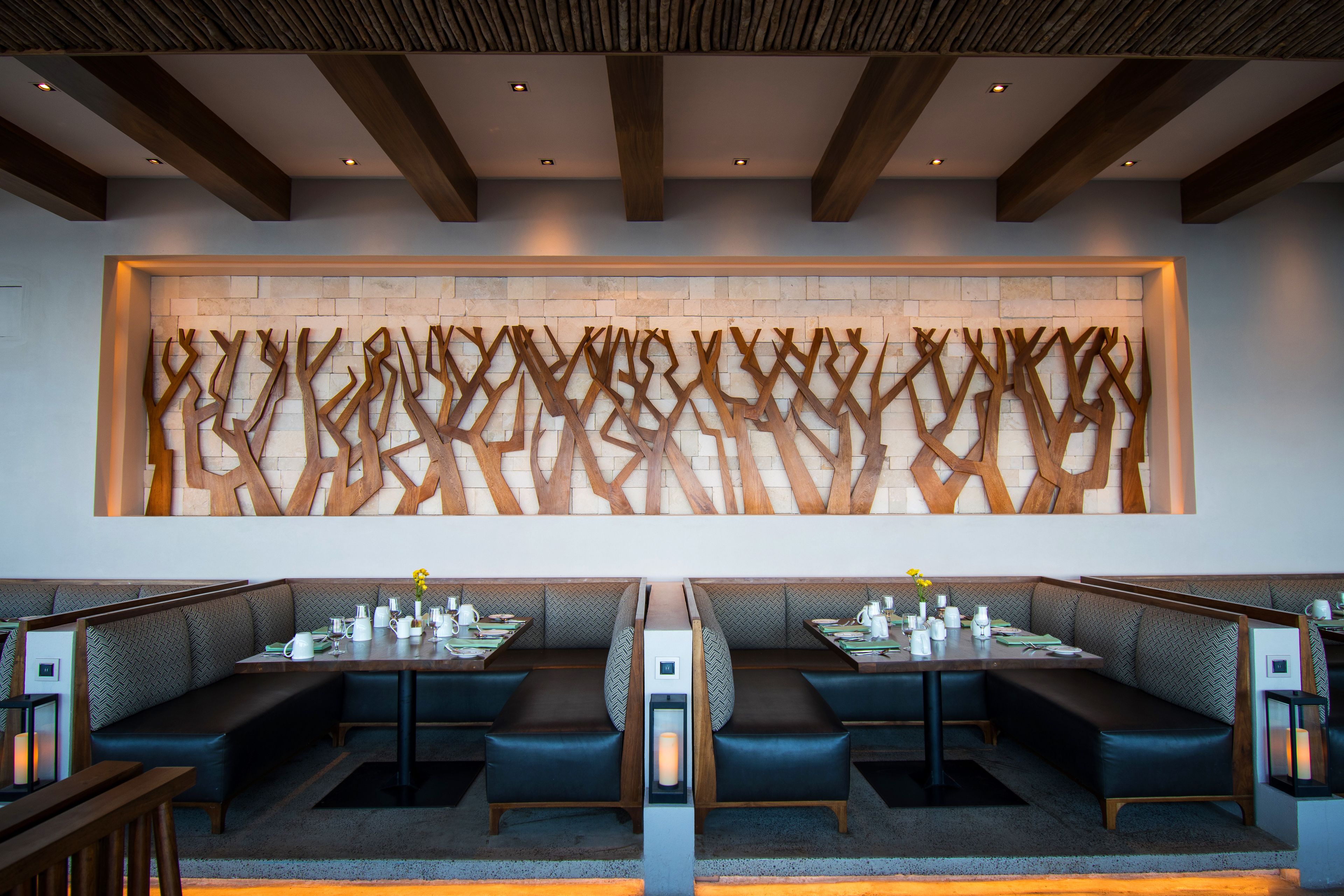 A modern restaurant with a central dining table flanked by booths, a decorative wall, and a wooden ceiling.