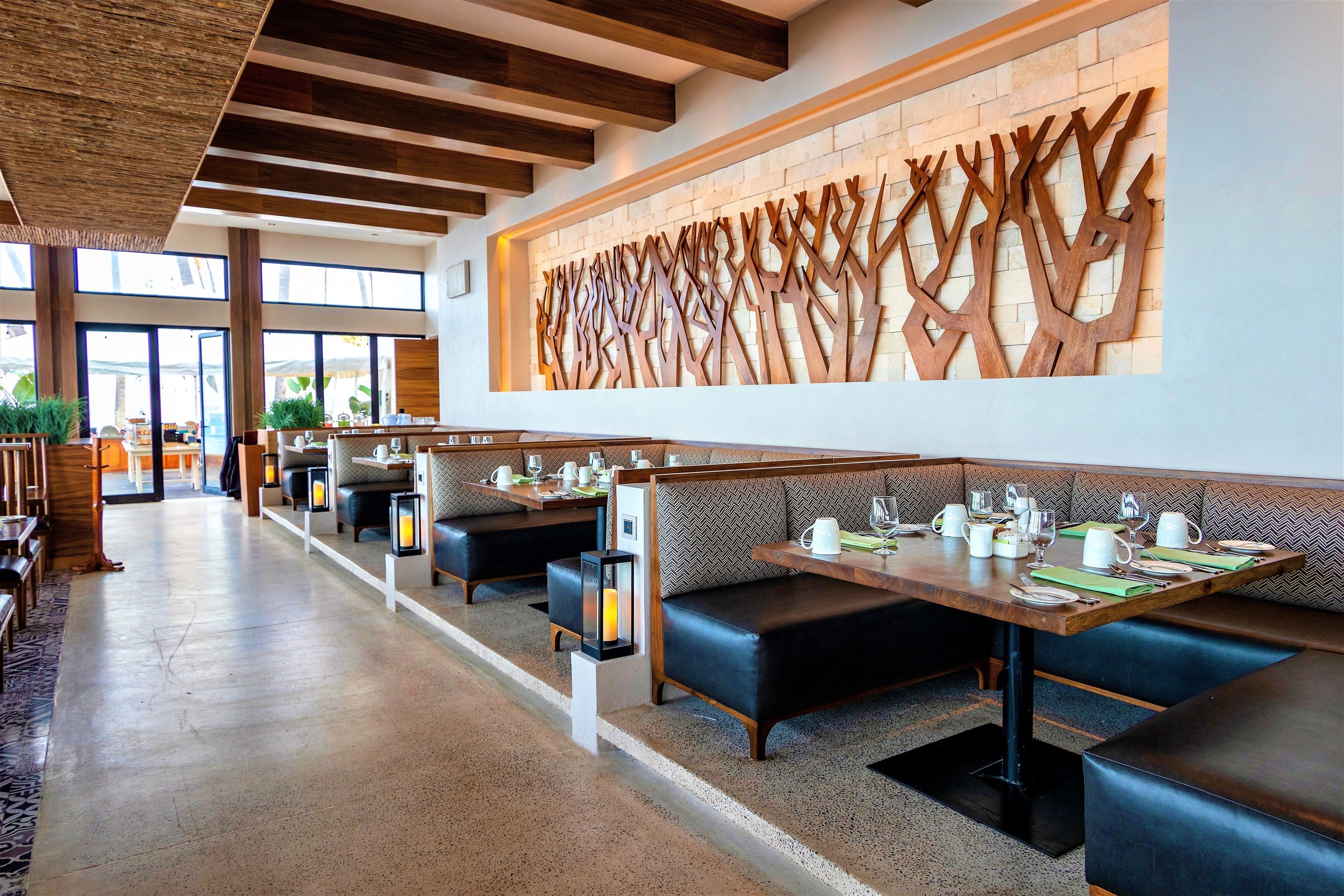 Un ristorante moderno con panche di legno, tavoli apparecchiati con posate e una parete decorativa.