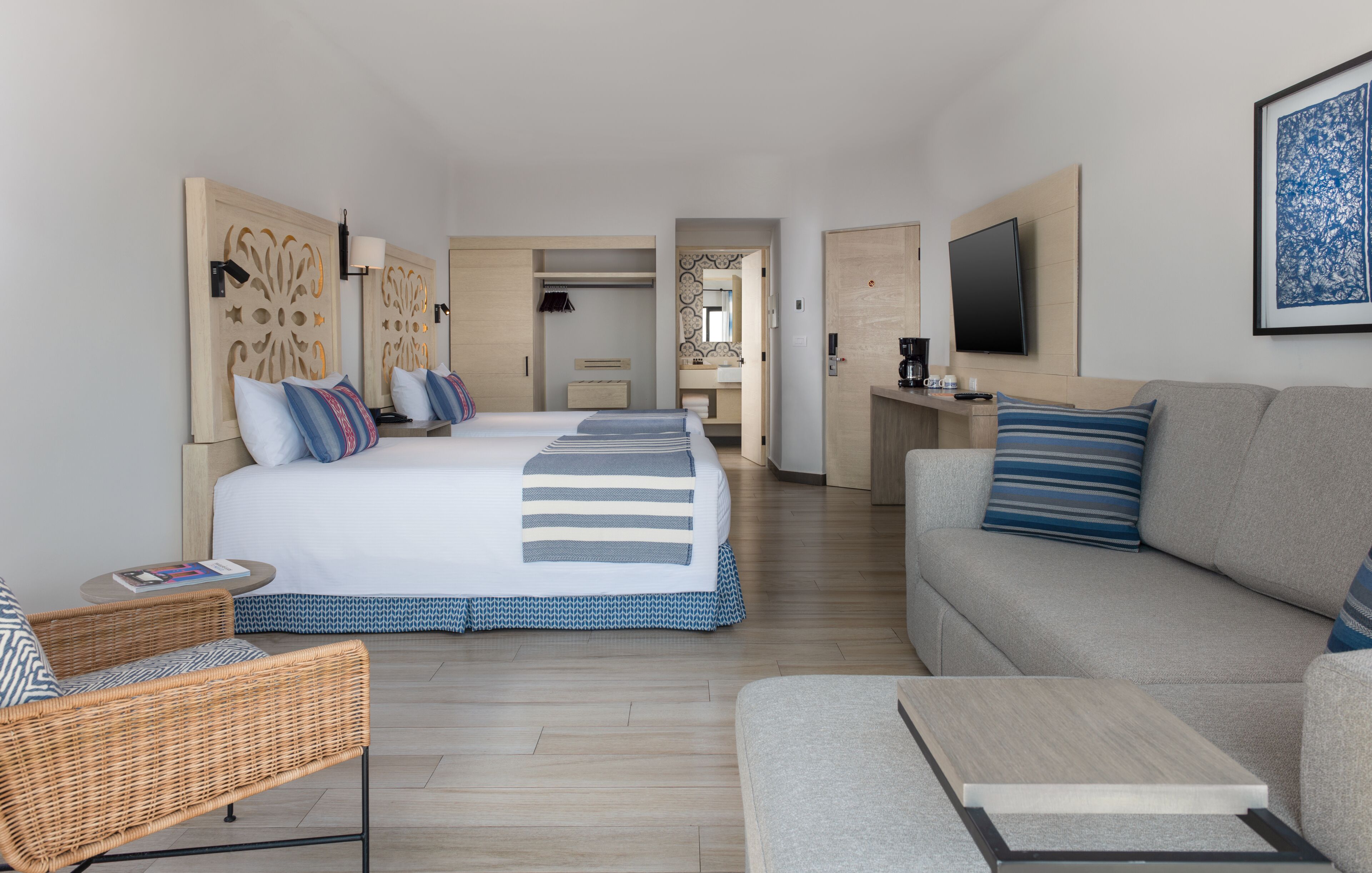 Une chambre d’hôtel avec un grand lit, un canapé, une table basse, un téléviseur et une salle de bain visible à travers une porte ouverte.