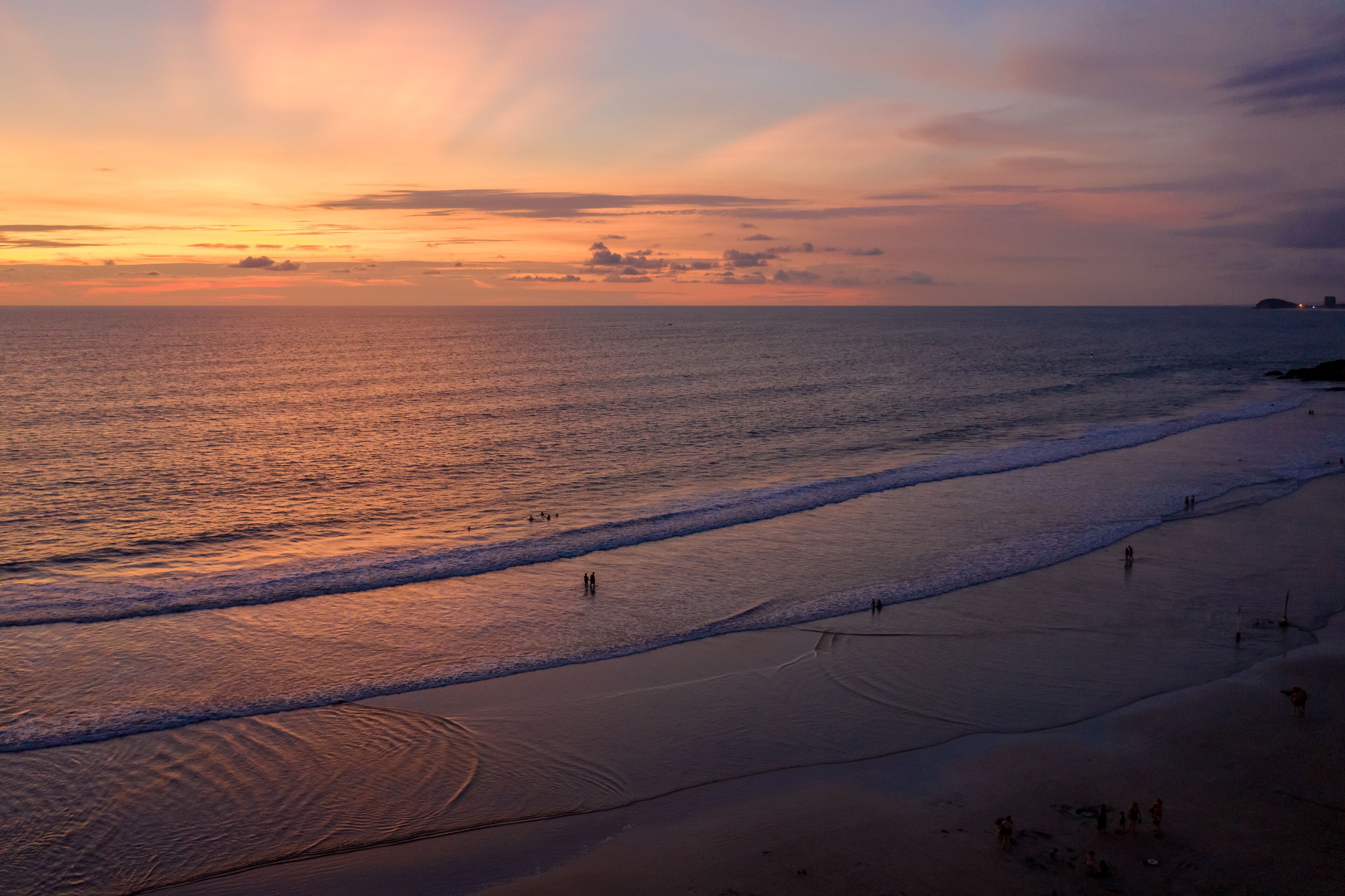 A beach with waves and people walking along the shore.