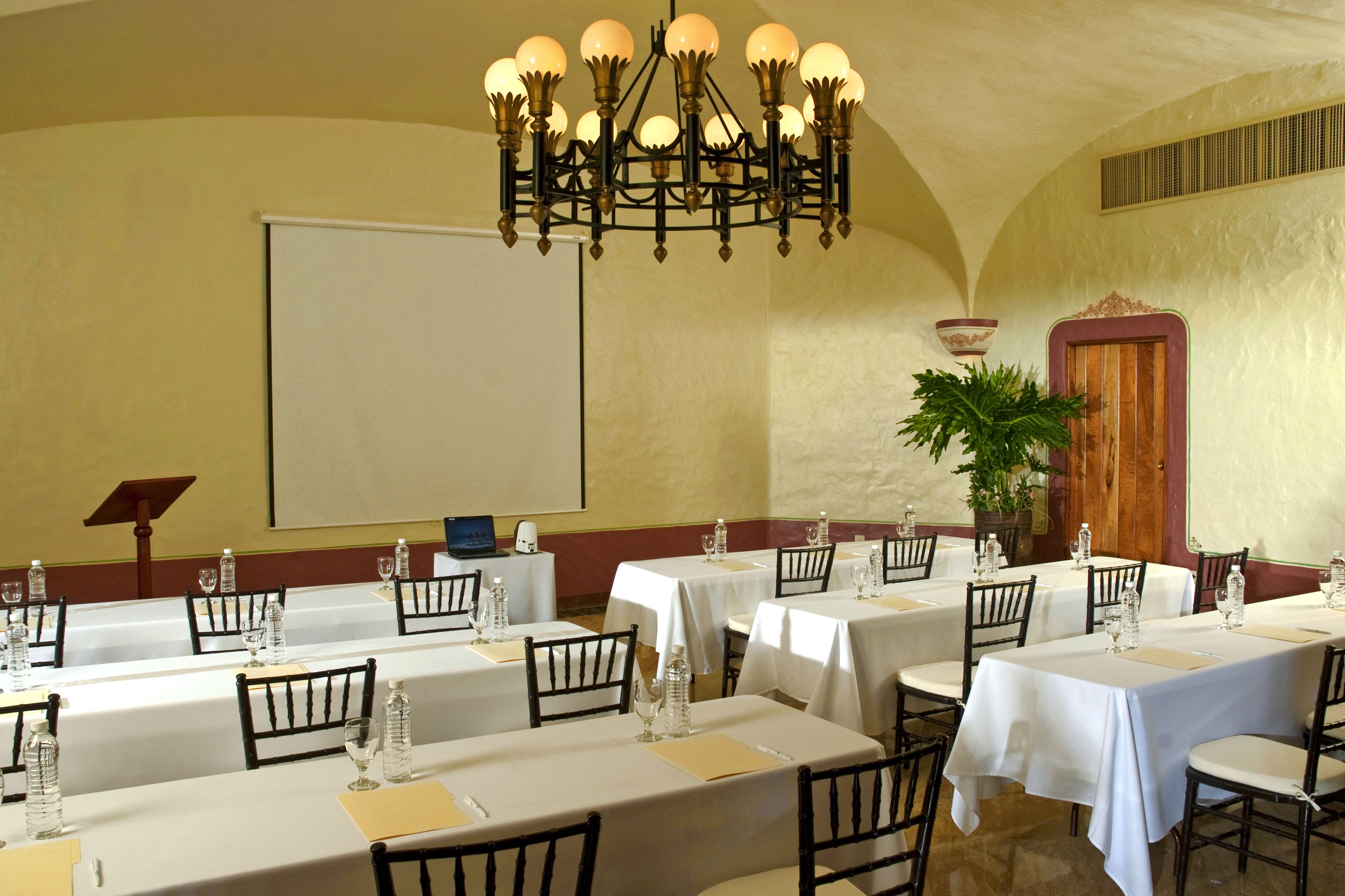 Una sala conferenze con diversi tavoli, sedie, uno schermo per proiettore e un lampadario.