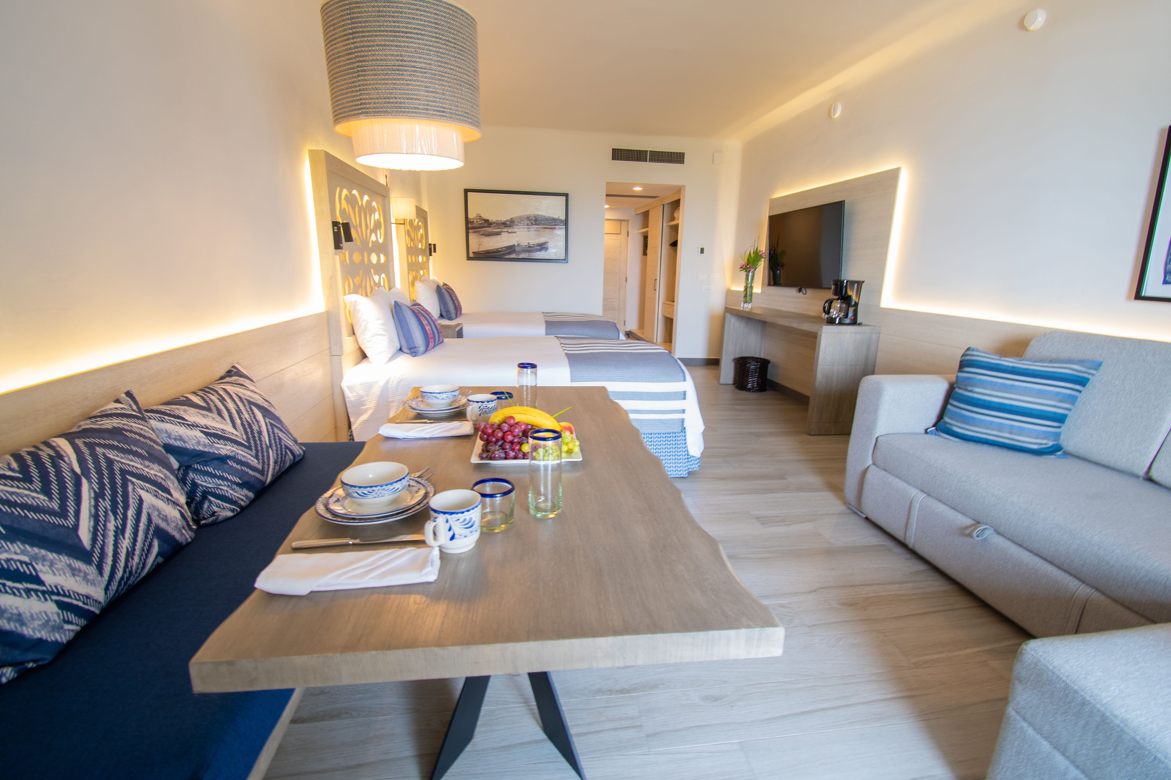 Una habitación de hotel moderna con zona de comedor, dos camas, un sofá y un televisor.