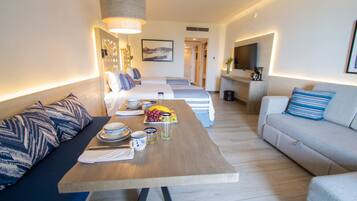 Una habitación de hotel moderna con zona de comedor, dos camas, un sofá y un televisor.