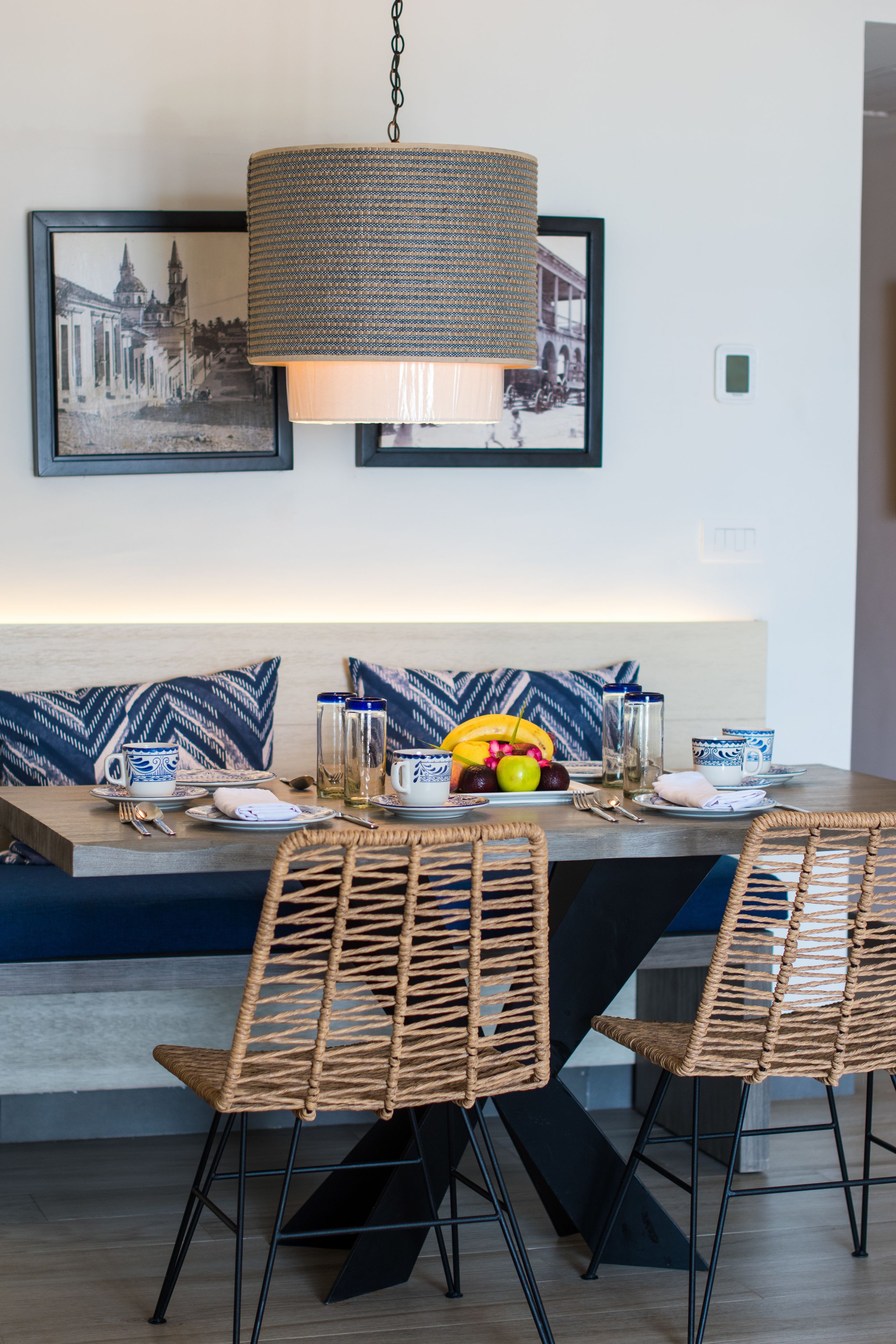 A dining area with wicker chairs, a table set for two, and a hanging lamp.