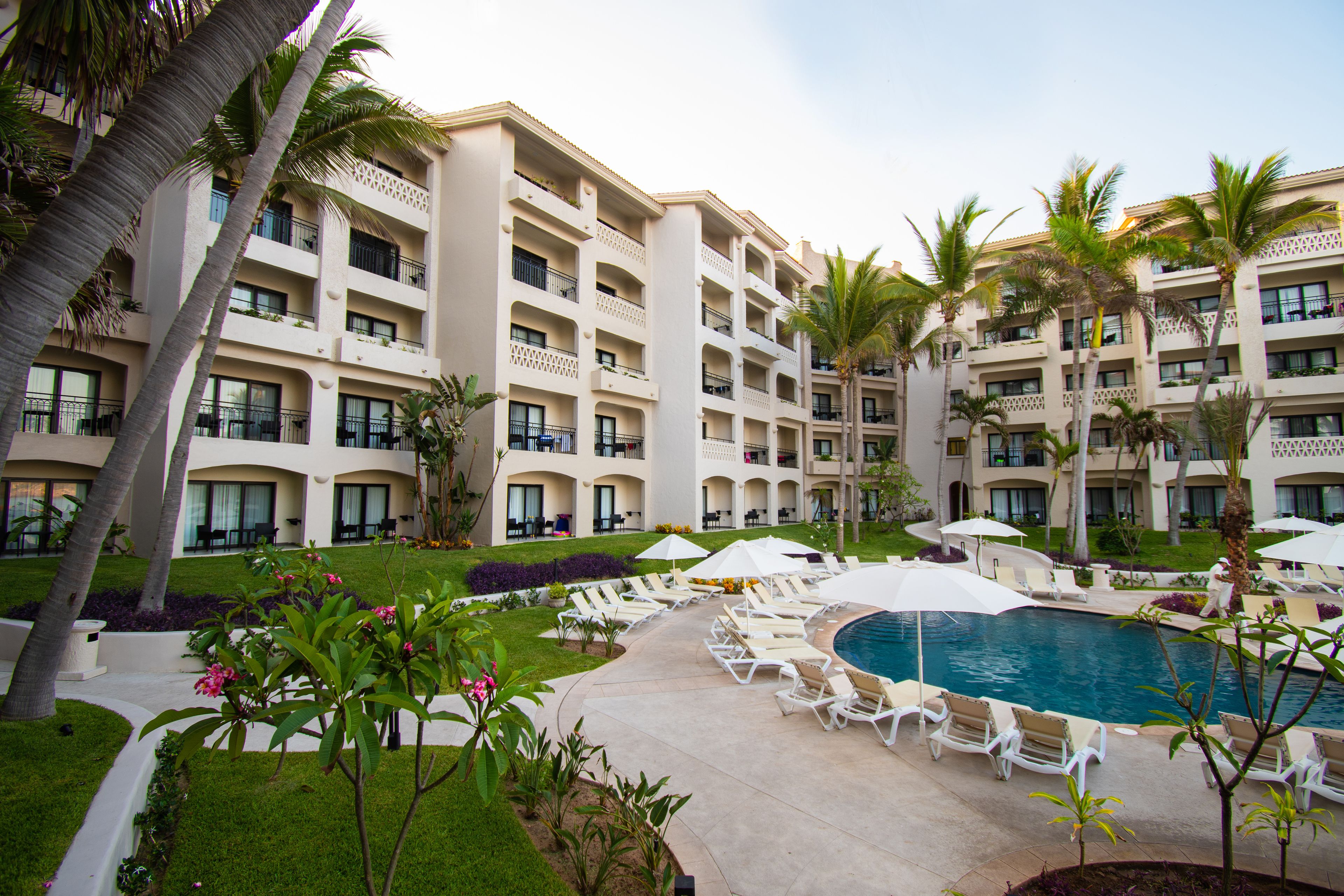 Un hotel con varios balcones, piscina y sillones de descanso.