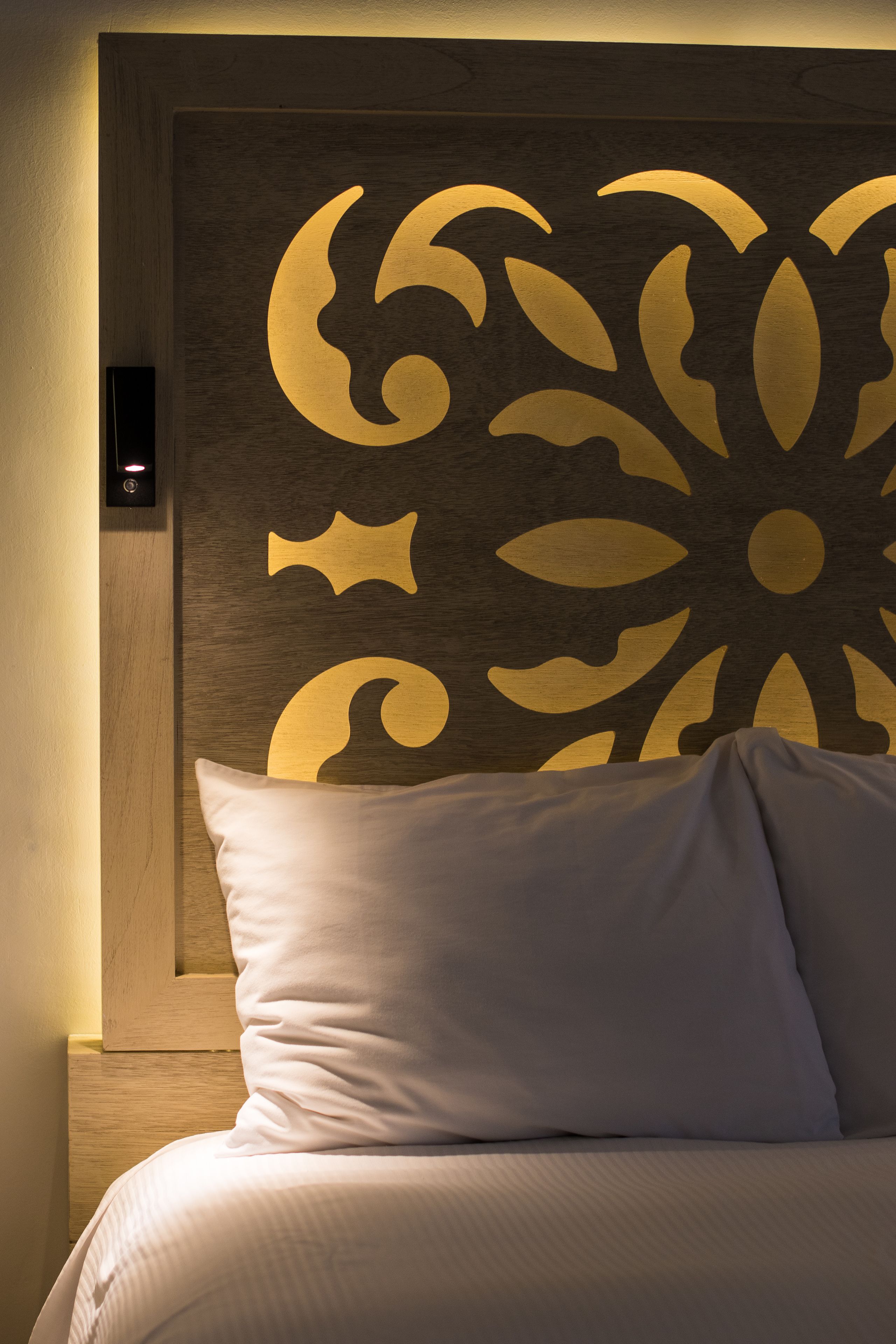 Una cama bien hecha con un cabecero que presenta un gran diseño floral estilizado.
