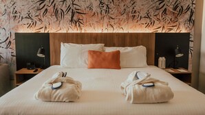 Una habitación de hotel con una cama grande, dos mesitas de noche, un cabecero de madera y una pared con un diseño de hojas.