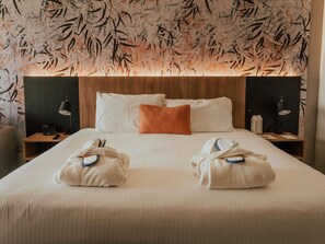 Una habitación de hotel con una cama grande, dos mesitas de noche, un cabecero de madera y una pared con un diseño de hojas.