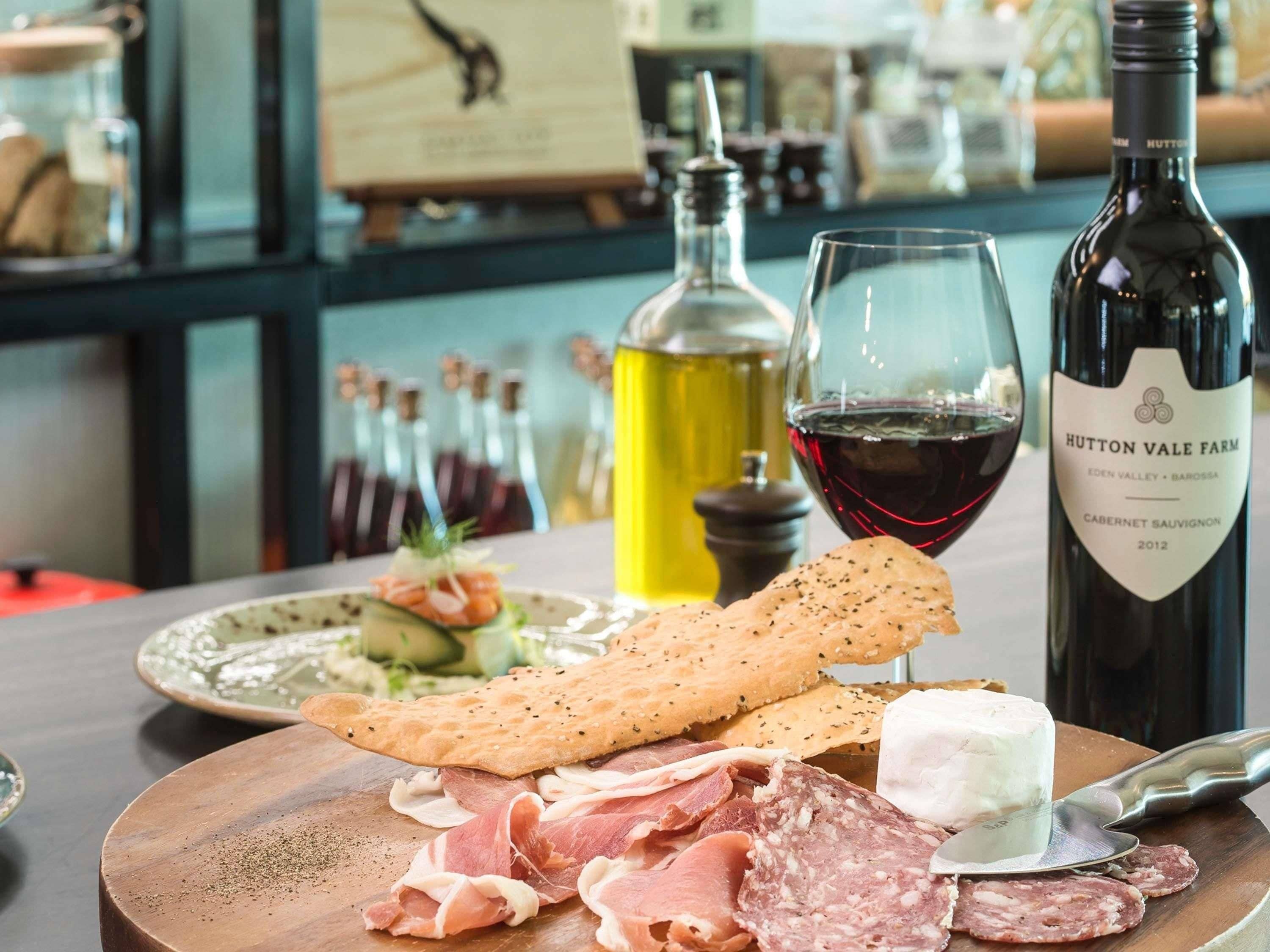 A charcuterie board with various meats, cheese, and crackers, a bottle of wine, and a glass of red wine on a wooden table.