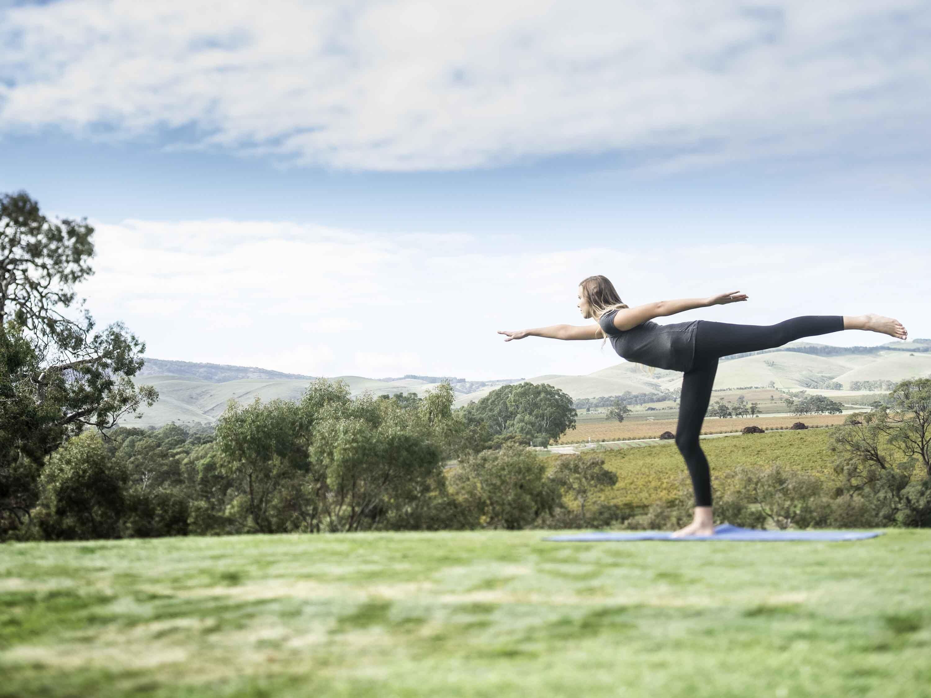 A person performing a yoga pose on a mat in an outdoor setting with a hilly landscape in the background.