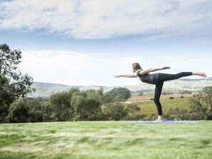 A person performing a yoga pose on a mat in an outdoor setting with a hilly landscape in the background. - Novotel Barossa Valley Resort (Rowland Flat)