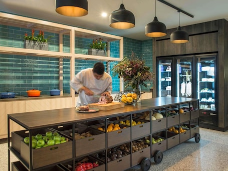 A chef preparing food in a modern kitchen with a fruit display and a refrigerated display case.
