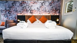 Una cama grande con sábanas blancas, dos almohadas naranjas y dos toallas dobladas sobre la cama.