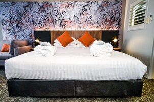 Una cama grande con sábanas blancas, dos almohadas naranjas y dos toallas dobladas sobre la cama.