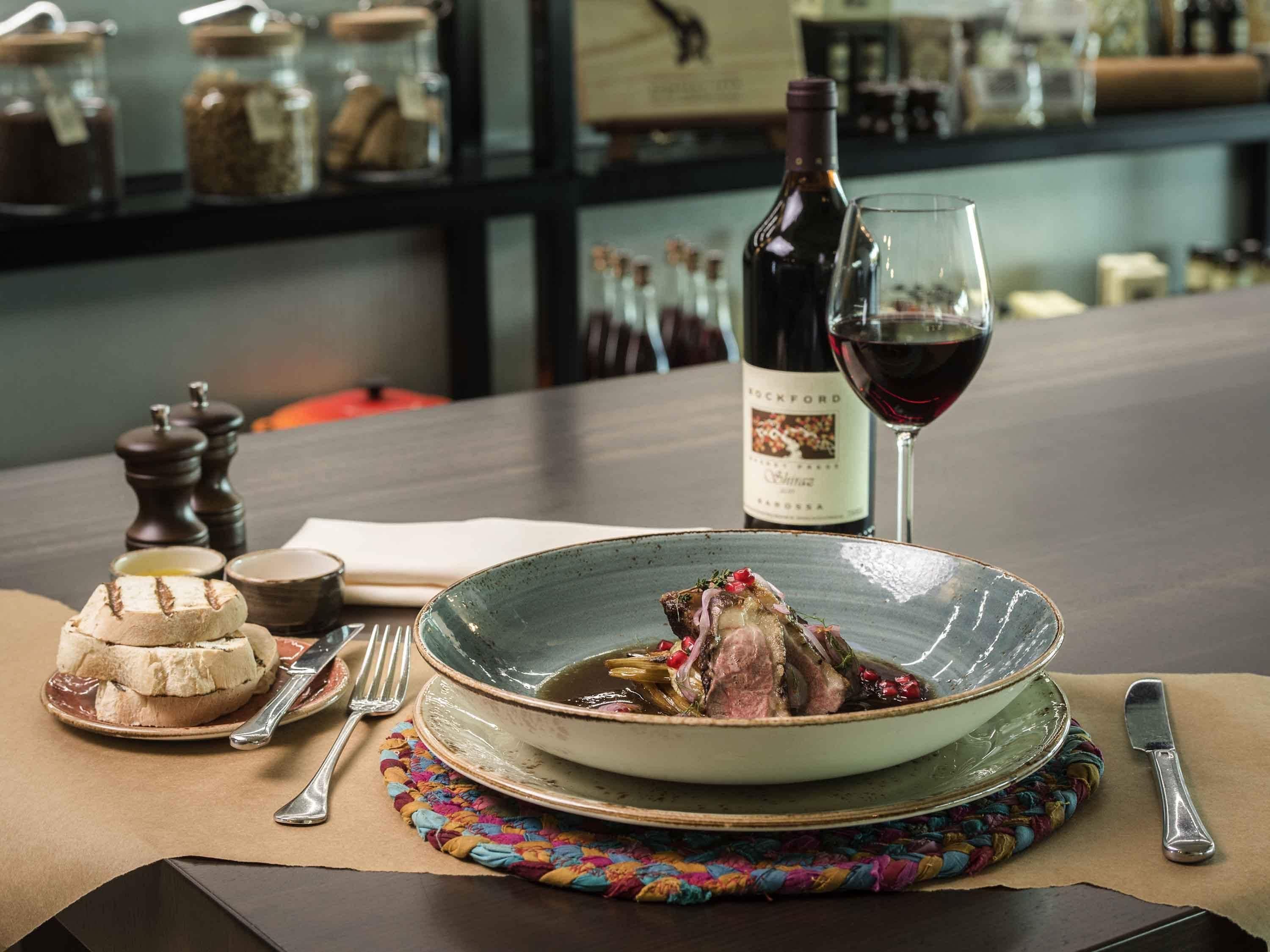 A dining table with a plate of food, a wine bottle, and a glass of red wine.