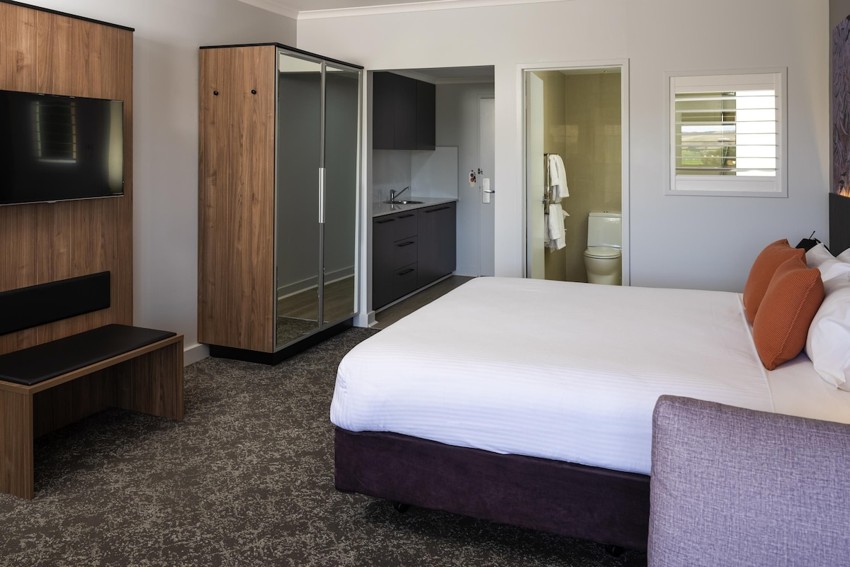 Una habitación de hotel moderna con una cama grande, televisión, armario, baño y una pequeña kitchenette.