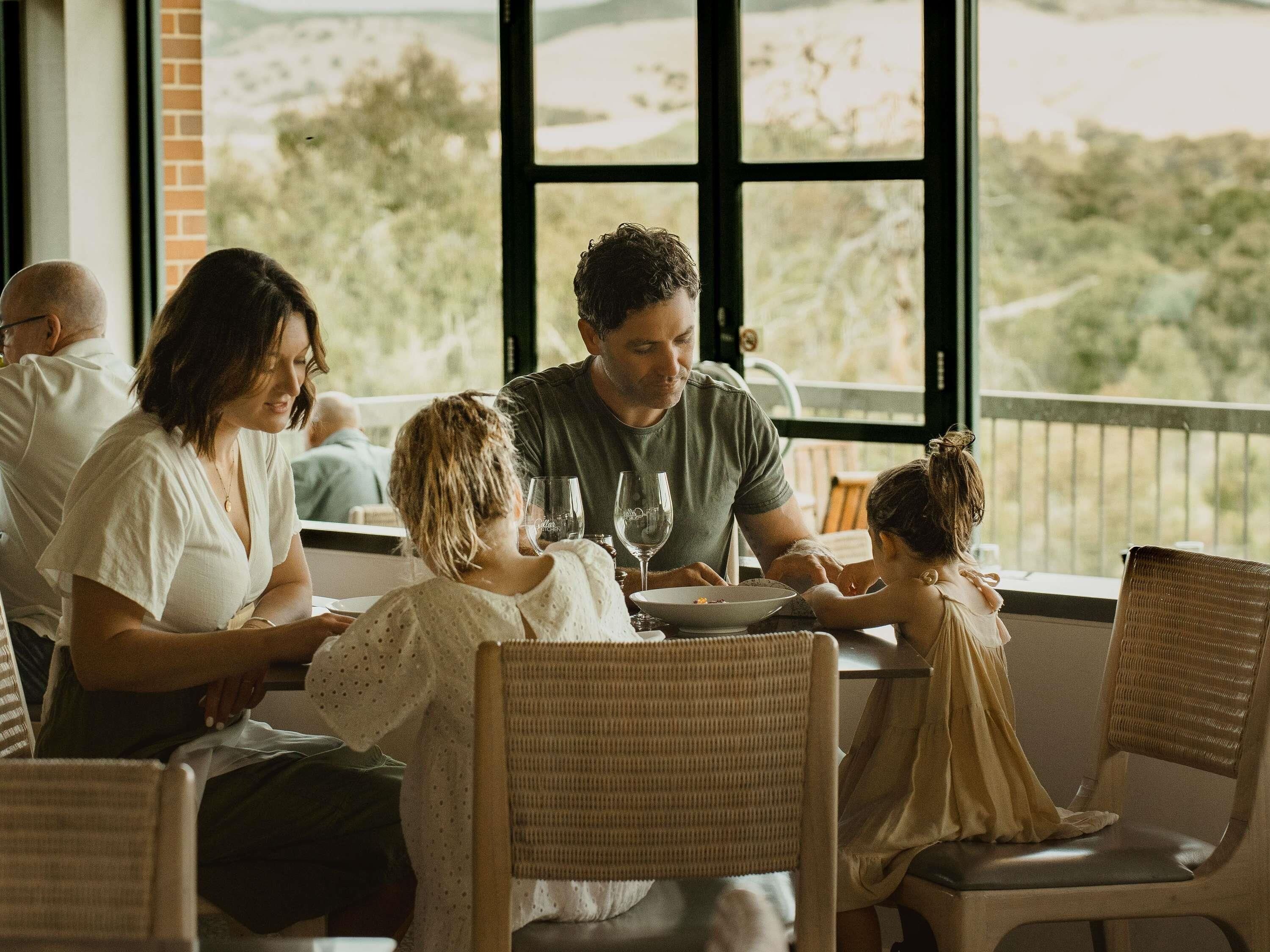 A family dining at a table with a view of a hilly landscape through large windows.