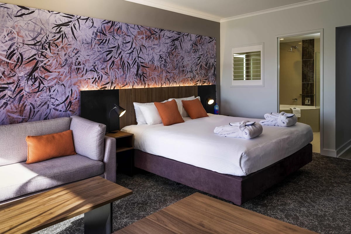 A hotel room with a bed, a sofa, a nightstand, and a bathroom visible through an open door.