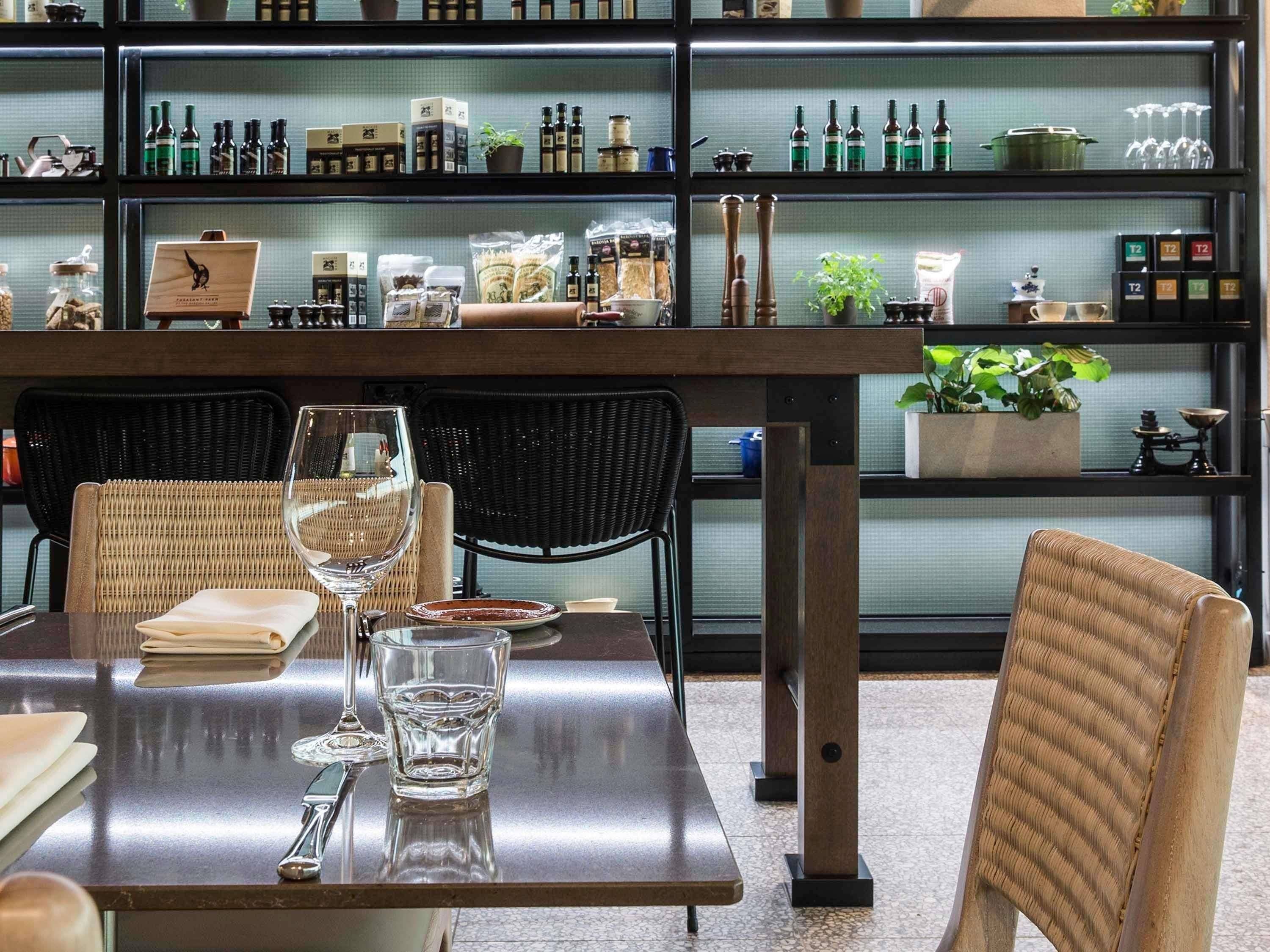 A dining area with a table set for two, chairs, and a shelf with various kitchen items in the background.