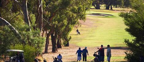 Un campo de golf con árboles, un carrito de golf y personas jugando.